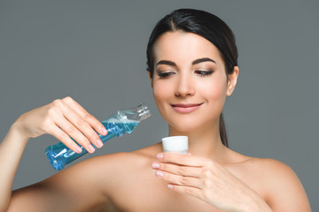 portrait of smiling woman with bare shoulders holding mouthwash isolated on grey