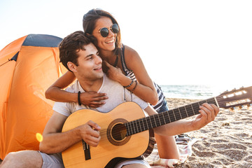 Sticker - Young cute loving couple play guitar on the beach outdoors.