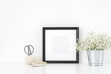 Black Frame Mockup In Interior With Vintage Elements . Frame Mock-Up Poster Or Photo Frame And Supplies On Table And Bouquet Of Flowers Near White Wall . Background