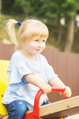 cheerful little blonde girl with two tails playing on the playground in summer sunny weather