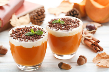 Pumpkin smoothie in glasses with cinnamon and acorns on wooden table