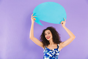 Sticker - Image of european woman with curly hair in dress smiling and holding blank bubble above her head with copyspace for your text, isolated over violet background in studio