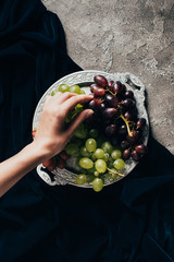 Wall Mural - partial top view of person eating delicious grapes from vintage plate