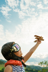 Happy kid playing with wooden toy airplane against blue summer sky background