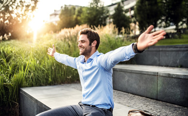 a happy young businessman with arms stretched outdoors at sunset.