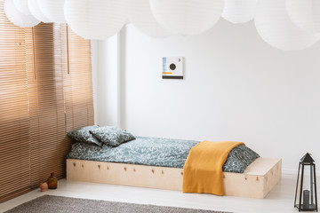 Poster - Orange blanket on wooden bed in white bedroom interior with lantern, poster and blinds. Real photo