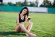 © lena_itzy - Young sporty joyful woman brunette in shorts and top sitting on the grass football field stadium and listens to music in earphones, her head thrown back, she gets pleasure, relaxes