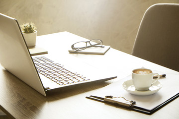 Wall Mural - Blank screen laptop computer, cup of cappuccino coffee, cactus, supplies and folded eye glasses on wooden desk in spacious office full of sunlight. Creative workspace. Close up, copy space, background