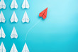 Leinwandbild Motiv Group of white paper plane in one direction and one red paper plane pointing in different way on blue background. Business for innovative solution concept.