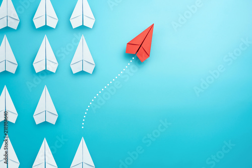 Fotomural Group of white paper plane in one direction and one red paper plane pointing in different way on blue background