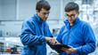 Two aircraft maintenance mechanics have a conversation while using a tablet in a plane hangar.
