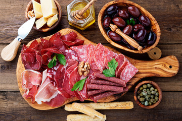 Antipasto platter cold meat with breadsticks, prosciutto, slices ham, beef jerky, salami and cheese platter on wooden board over rustic background. 