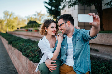 Wall Mural - Collecting the bright moments. Smiling young couple making selfie while sitting outdoors.