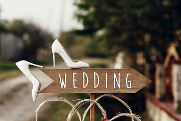beautiful white shoes on wooden arrow with wedding text sign. rustic wedding concept. pointing for wedding ceremony location. creative ideas