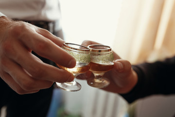 hands of man holding glasses with vodka and toasting. group of men cheering and clinking with drinks at wedding reception