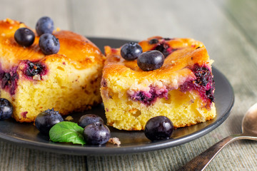 Two pieces of blueberry cake on a dark saucer.