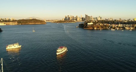 Wall Mural - Over still waters of Sydney harbour above moored yachts towards distant Sydeny city CBD landmarks in aerial ascending.
