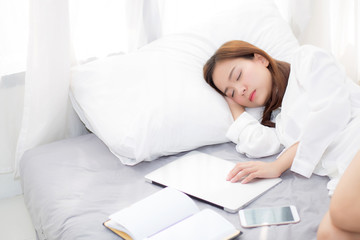 Beautiful young asian woman with laptop lying down in bedroom, girl tired sleep with computer notebook and smart mobile phone, resting and healthcare concept.