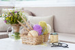 Wool and cotton yarn in a wicker basket on a white table in a light interior. A bouquet of wild flowers.