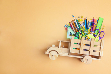 Back to school concept with wooden toy truck with school supplies on yellow background and copy space.