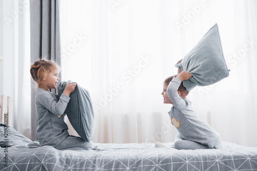 Little Boy And Girl Staged A Pillow Fight On The Bed In The