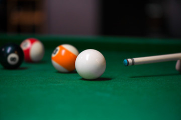 Wall Mural - Sport billiard balls on green billiard table in pub. Player is about to hit the ball, focusing on his shot. On going billiard game. Competitive players trying to find out the winner of the round.