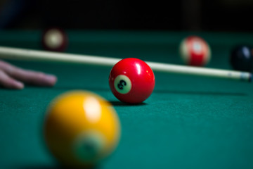 Wall Mural - Sport billiard balls on green billiard table in pub. Player is about to hit the ball, focusing on his shot. On going billiard game. Competitive players trying to find out the winner of the round.