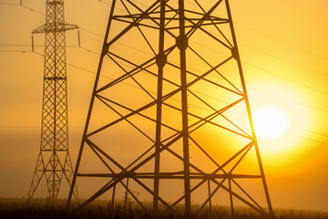 High voltage transmission towers in meadow at orange sunset 
