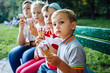 © Iryna - Group of four happy children eating ice cream together outdoor. Photo of happy blond girls with two handsome boys sitting on the bench and smiling at camera.