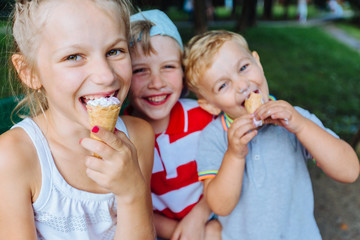 team of three different age happy children eating ice-cream and having fun together outdoors in park