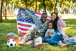 © LIGHTFIELD STUDIOS - Happy African American soldier in military uniform and family holding American flag in park