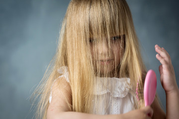 Wall Mural - little blonde girl with long hair combs her hair with a pink comb