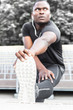 © xartproduction - Concentrated african american sportsman warming up and stretching legs on pier