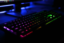 Close Up View Of Workplace With Led Rainbow Backlight Gaming Keyboard Of Computer, Lying On Table In Dark Room