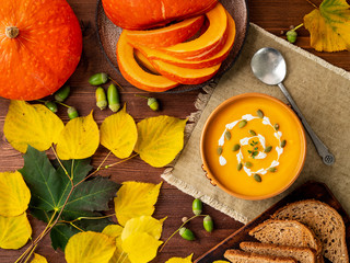 Wall Mural - Autumn food. Pumpkin puree soup, leaves, dark brown old wooden table, top view.