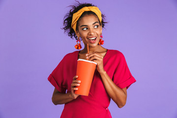 Poster - Cheerful african woman in dress drinking soda from paper cup