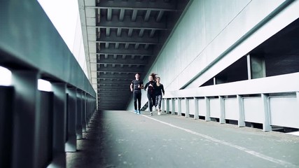 Wall Mural - Young athlete friends running under the bridge in the city.