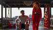 Beautiful Red-Haired Girl Rolls Guy In A Wheelchair On The Promenade In The Evening