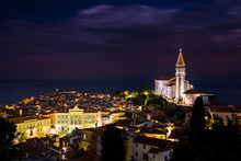 Night Cityscape Of City Of Piran, Slovenia With Big Dominant St. George's Parish Church And Main Square