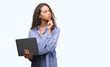 © Krakenimages.com - Young hispanic woman holding computer laptop serious face thinking about question, very confused idea