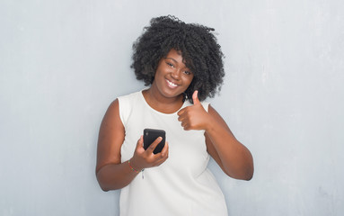 Canvas Print - Young african american woman over grey grunge wall texting a message using smartphone happy with big smile doing ok sign, thumb up with fingers, excellent sign