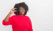© Krakenimages.com - Young african american plus size woman over white brick wall smiling and confident gesturing with hand doing size sign with fingers while looking and the camera. Measure concept.