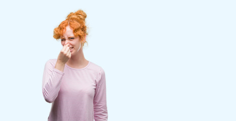 Poster - Young redhead woman smelling something stinky and disgusting, intolerable smell, holding breath with fingers on nose. Bad smells concept.