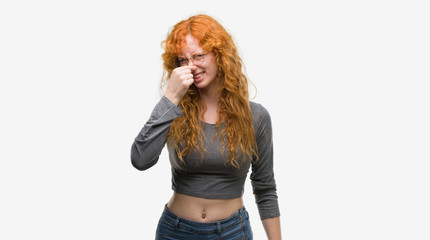 Poster - Young redhead woman smelling something stinky and disgusting, intolerable smell, holding breath with fingers on nose. Bad smells concept.