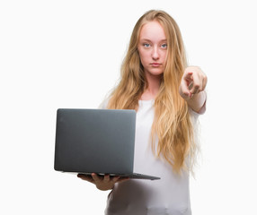 Sticker - Blonde teenager woman using computer laptop pointing with finger to the camera and to you, hand sign, positive and confident gesture from the front