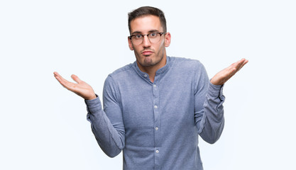 Canvas Print - Handsome young elegant man wearing glasses clueless and confused expression with arms and hands raised. Doubt concept.