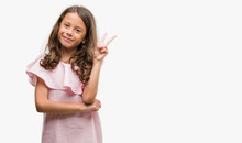 Brunette Hispanic Girl Wearing Pink Dress Smiling With Happy Face Winking At The Camera Doing Victory Sign. Number Two.