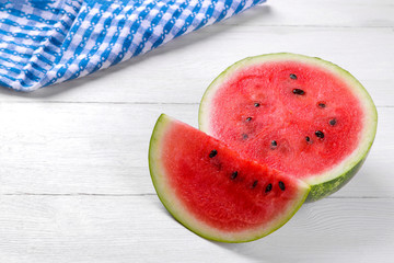 A large ripe red watermelon next to a slice on a white wooden table with a place for inscription