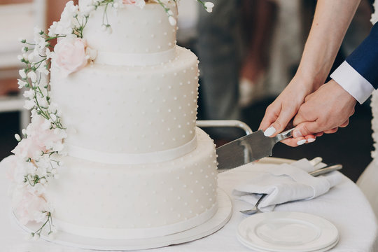 bride and groom holding knife and cutting stylish white wedding cake with flowers. modern big weddin