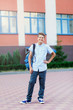 © Natali - cute, young boy in blue shirt stands  in front of school with blue backpack and thumb up. Education, back to school concept